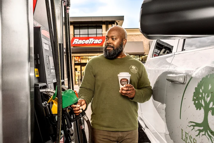 man pumping RaceTrac diesel fuel and holding a Crazy Good Coffee